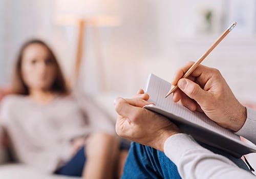 therapist writes on notepad as woman talks about an opioid addiction treatment program